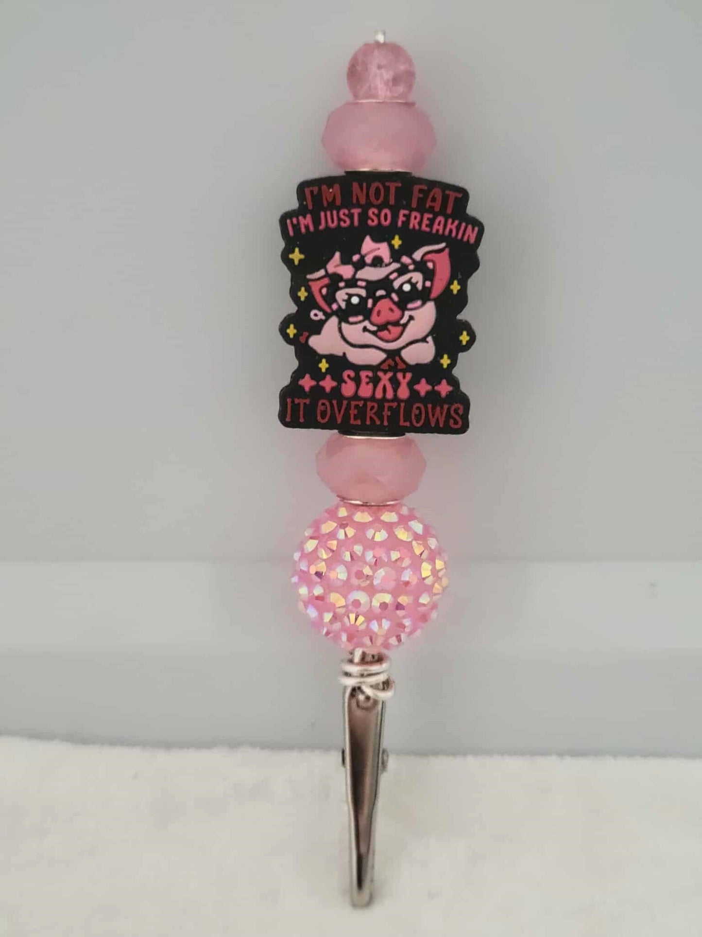 Decorative joint holder. Pink roach clip with a silicone bead showing a pink pig on glasses with the words written "I'm not fat I'm just so freaking sexy it overflows", along with shimmering pink beads and one chunky pink sparkling bubblegum bead.
