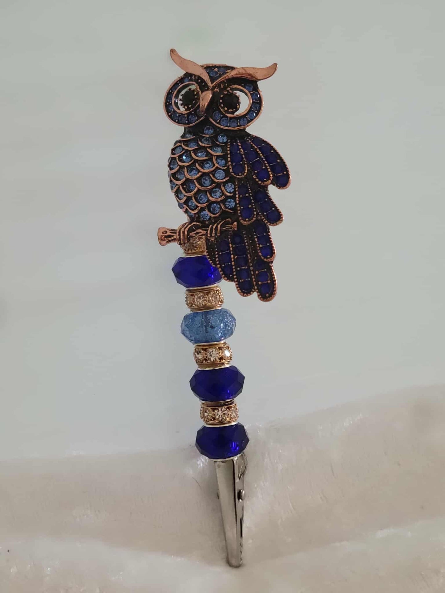 Decorative joint holder. Sapphire-toned owl roach clip perched atop a string of shimmering blue and gold beads.