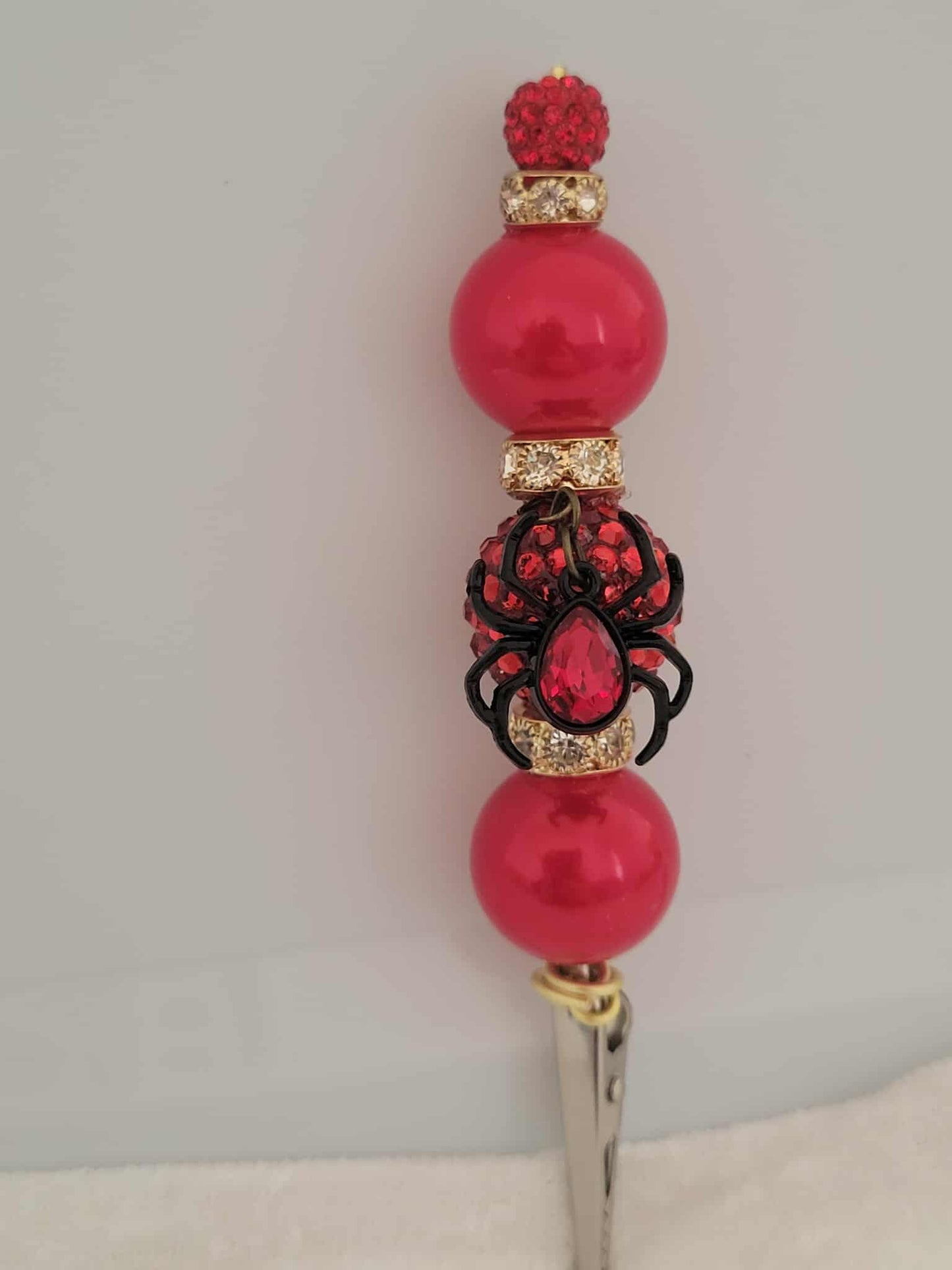 Decorative joint holder. Sultry red roach clip featuring a jeweled black widow charm with a red jewel in the center, wrapped in crimson beads and gold accents.