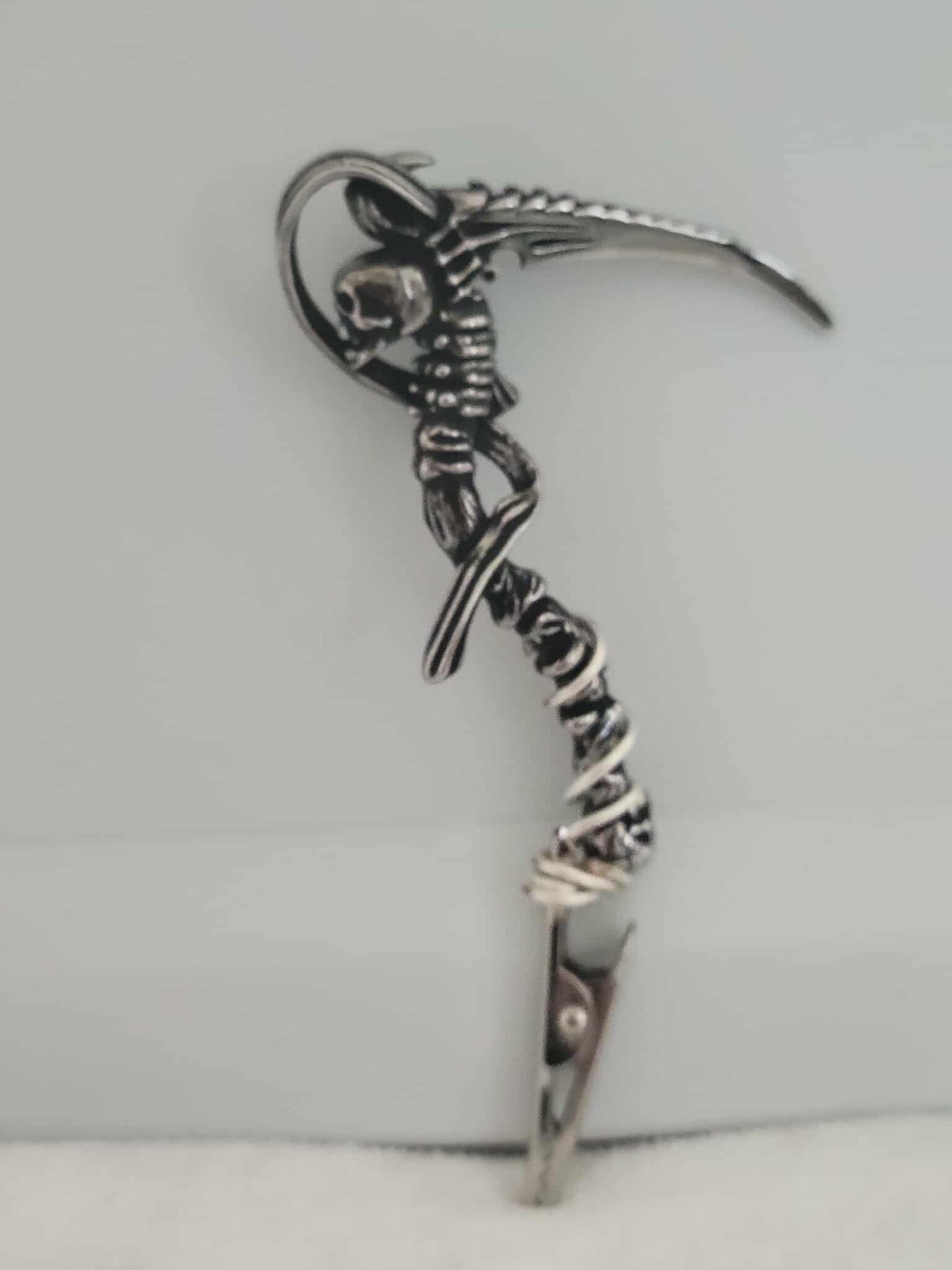Decorative joint holder. Grim Reaper roach clip. Silver skull connecting to the spinal cord, holding a scythe, and wire wrapped into the clip.