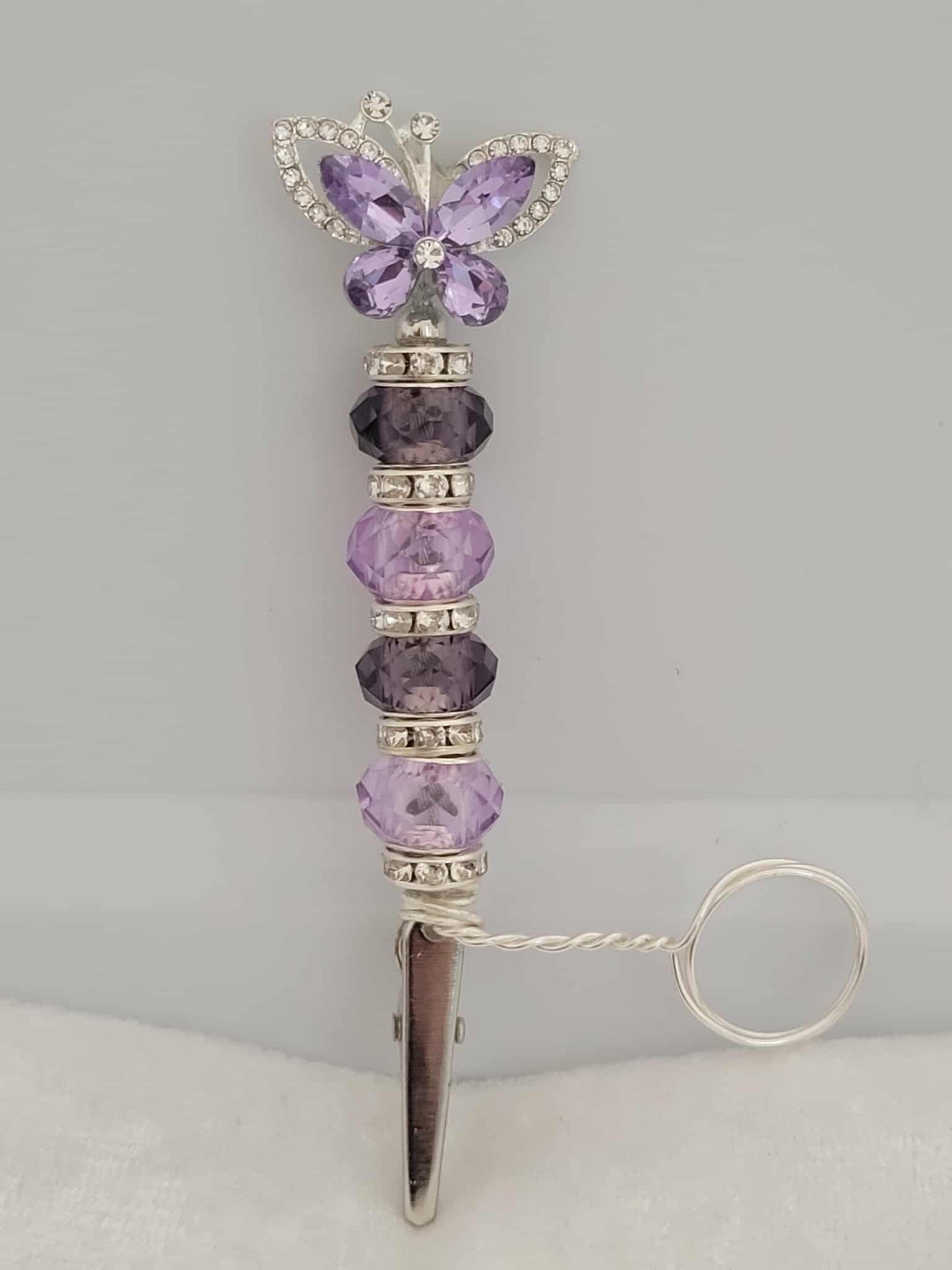 Handcrafted silver and purple roach clip. With rhinestone spacers.  There is a metal ring extending from right above the roach clip and below the start of the beads. This allows users to wear the ring on their finger that holds the roach clip allowing the user to hold other objects like your phone or a video game controller.  The ring is not adjustable and was made to be worn as a midi-ring, about a midi ring size 3 (14mm)