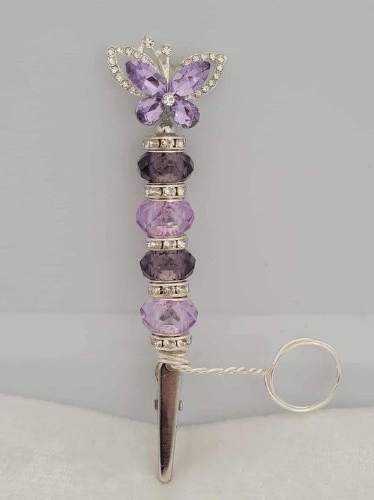 Handcrafted silver and purple roach clip. With rhinestone spacers.  There is a metal ring extending from right above the roach clip and below the start of the beads. This allows users to wear the ring on their finger that holds the roach clip allowing the user to hold other objects like your phone or a video game controller.  The ring is not adjustable and was made to be worn as a midi-ring, about a midi ring size 3 (14mm)