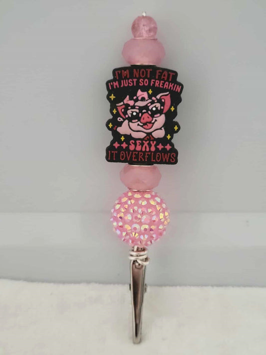Decorative joint holder. Pink roach clip with a silicone bead showing a pink pig on glasses with the words written "I'm not fat I'm just so freaking sexy it overflows", along with shimmering pink beads and one chunky pink sparkling bubblegum bead.