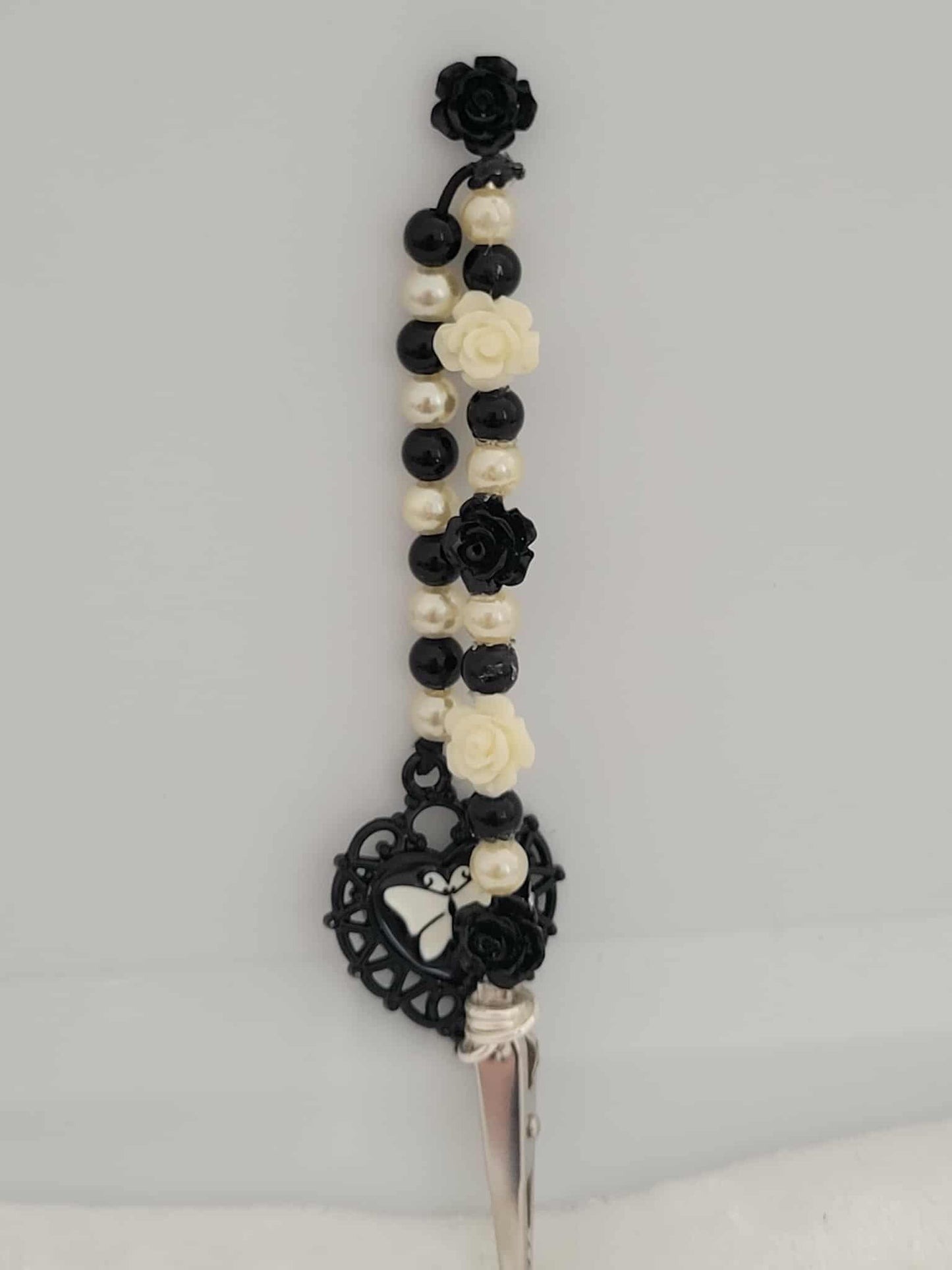 Decorative joint holder. Gothic handcrafted roach clip blends vintage charm with gothic flair, featuring black and ivory rose beads, faux pearls, and an ornate heart charm with a butterfly silhouette