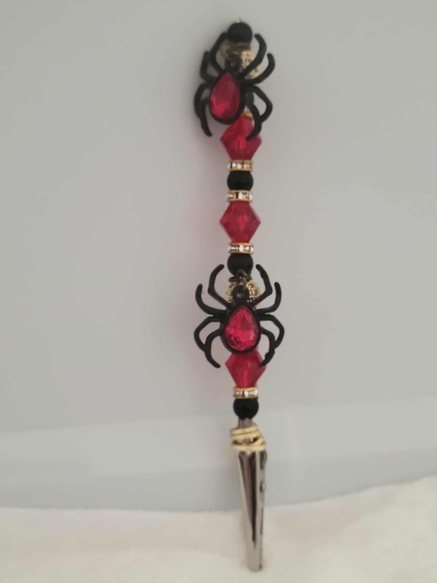 Decorative joint holder. This handcrafted roach clip is crawling with red and black shimmering gems and double black widow charms, each with a red jeweled stone in the center.