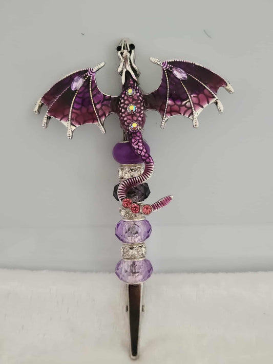Decorative joint holder. Handmade dark purple dragon roach clip that has jewels on its wings, body and tail. On the handle there are two light purple beads, one amethyst bead, one blackish purple bead and silver rhinestone spacers.