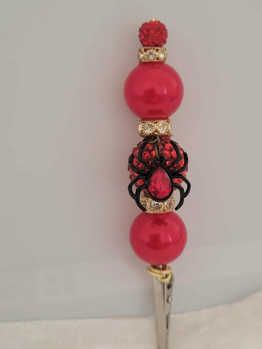 Decorative joint holder. Sultry red roach clip featuring a jeweled black widow charm with a red jewel in the center, wrapped in crimson beads and gold accents.