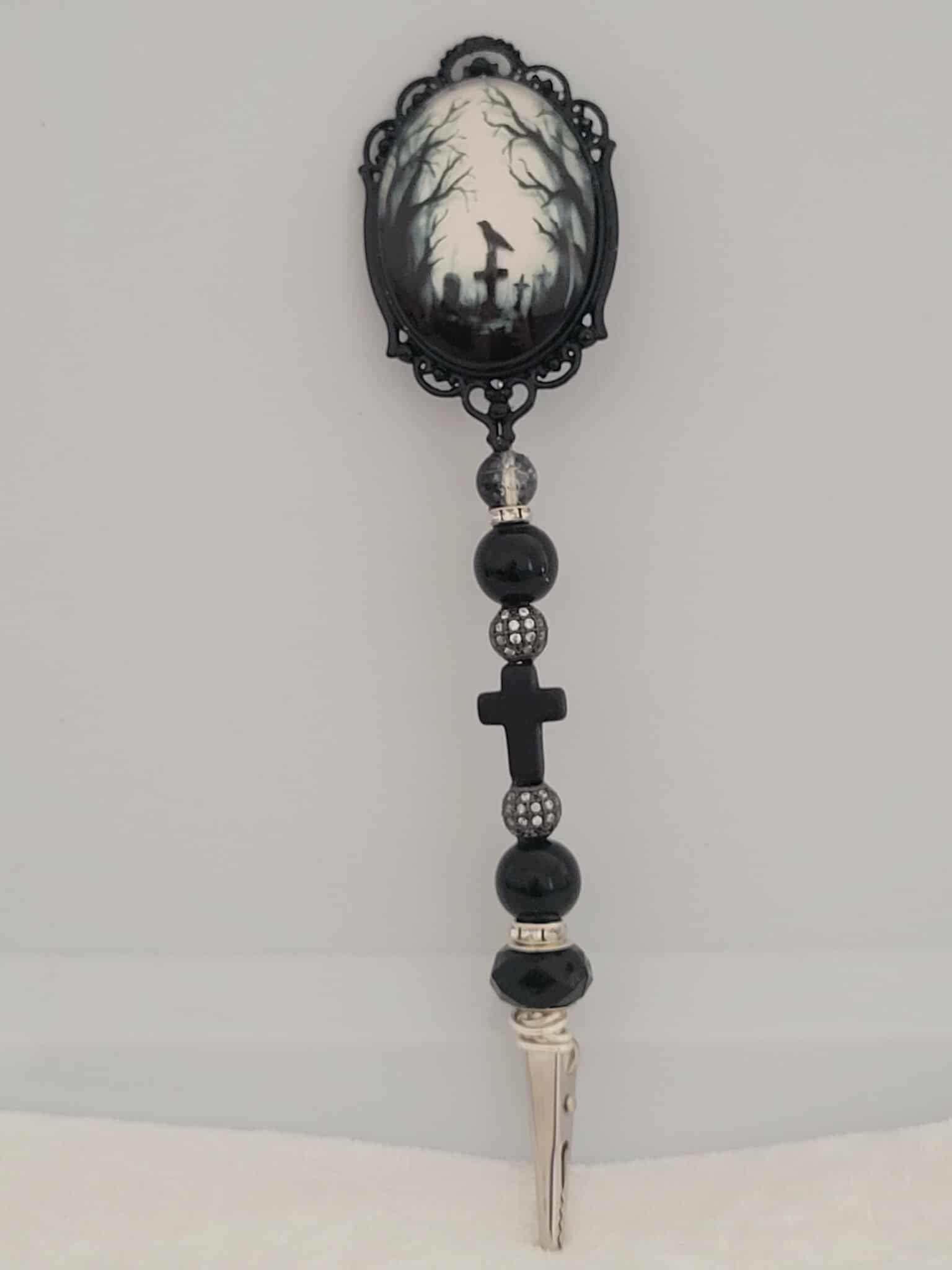 Decorative joint holder. Gothic handcrafted roach clip featuring a gothic cameo centerpiece of a graveyard scene including gravestones, crosses, black crows and spooky forest. With dark faceted beads, shimmering black rhinestone spacers, and a matte cross bead.