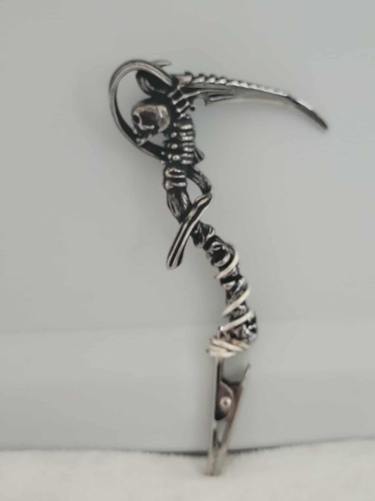 Decorative joint holder. Grim Reaper roach clip. Silver skull connecting to the spinal cord, holding a scythe, and wire wrapped into the clip. 